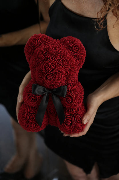 Red rose teddy bear presented with both hands against a black dress
