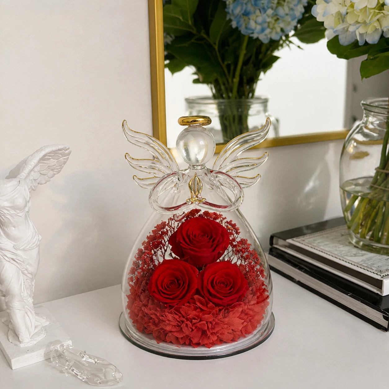 Großer Glasengel mit drei roten Rosen auf einer eleganten weißen Konsole