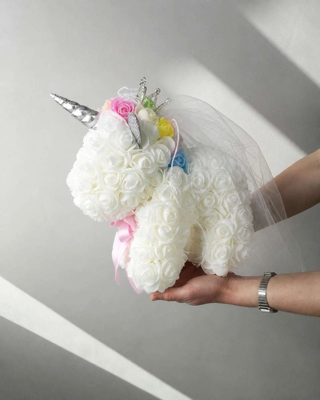 White rose unicorn keepsake held by a softly lit window