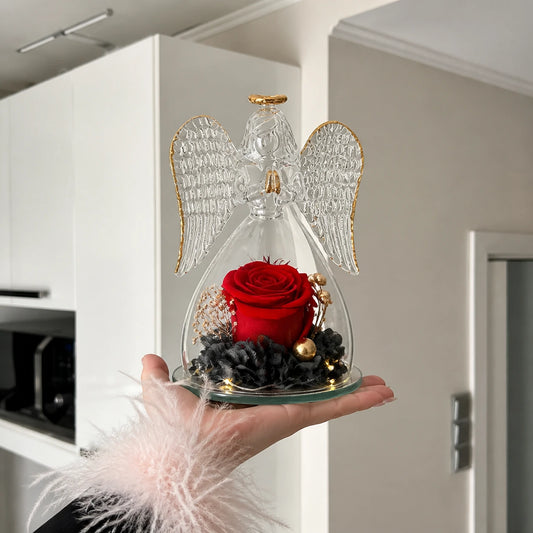 Hand hält einen kleinen Glasengel mit einer roten Rose in einer hellen Küche
