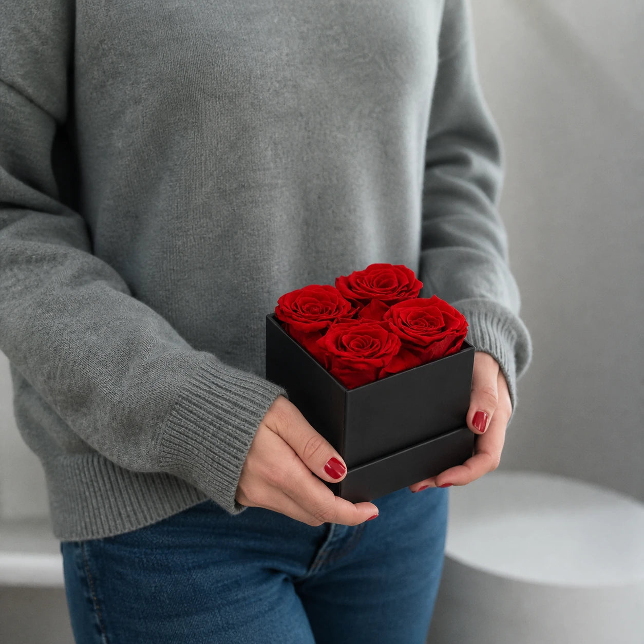 Hand hält eine schwarze Geschenkbox mit vier roten konservierten Rosen
