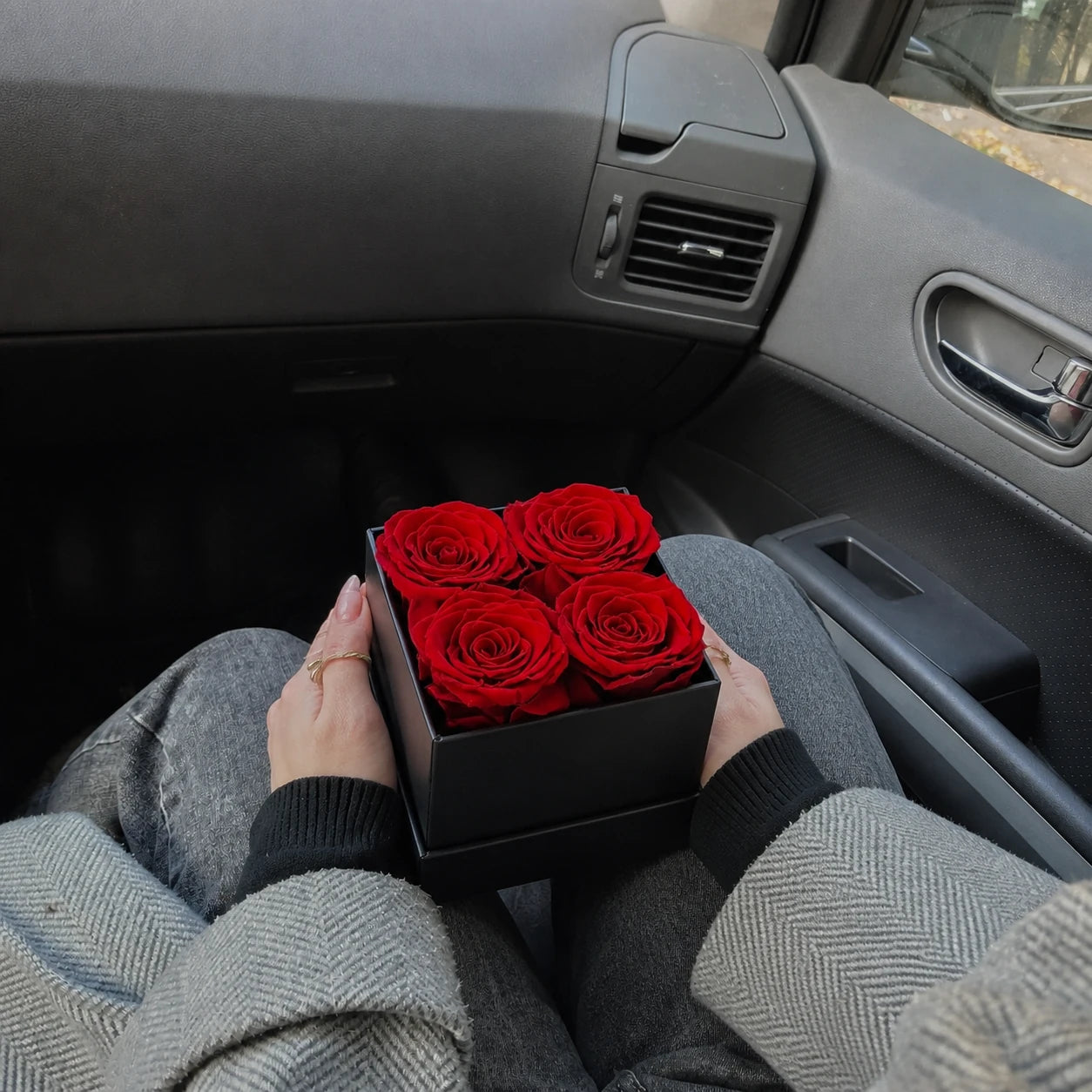 Schwarze Geschenkbox mit vier roten konservierten Rosen auf einem Bett