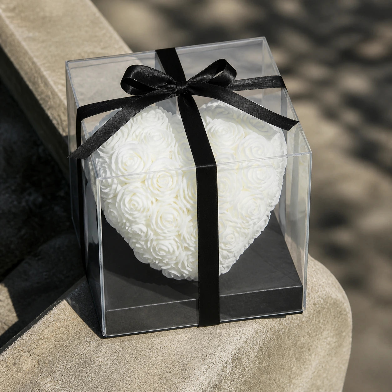 Weißes Rosenherz in transparenter Geschenkbox auf einer sonnigen Steinkante