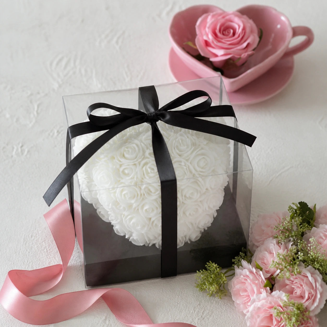 Weißes Rosenherz in transparenter Geschenkbox mit rosafarbenen Blumen