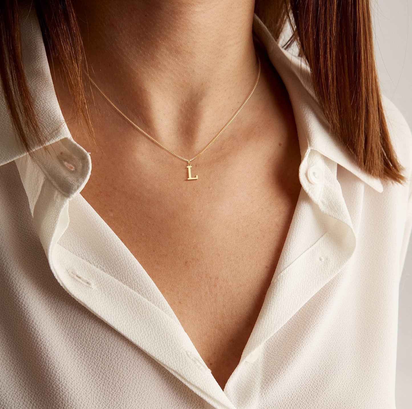 Eine Frau trägt die Swaravo  Minimal Serif Initialen-Halskette zu einem schlichten, eleganten Outfit – perfekt für den Alltag.