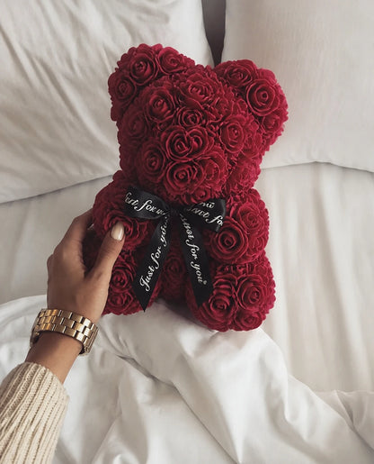 Red rose teddy bear held beside a softly styled bed